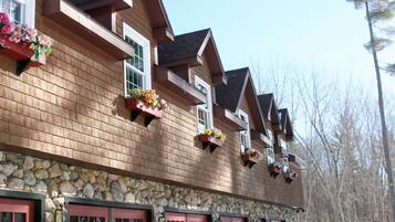 A wooden building with multiple windows and balconies, stone foundation, and red garage doors.