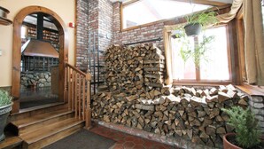 A wooden staircase leading to a loft area with a brick fireplace, a large window with a plant, and a stone wall with stacked firewood. - The Old Saco Inn (Fryeburg)