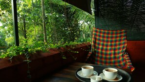 A cozy seating area with a wooden bench and a chair, a tray with two cups of coffee, and a view of lush greenery through a window. - Grassroots Wayanad, Valley-view Tents (Vythiri)