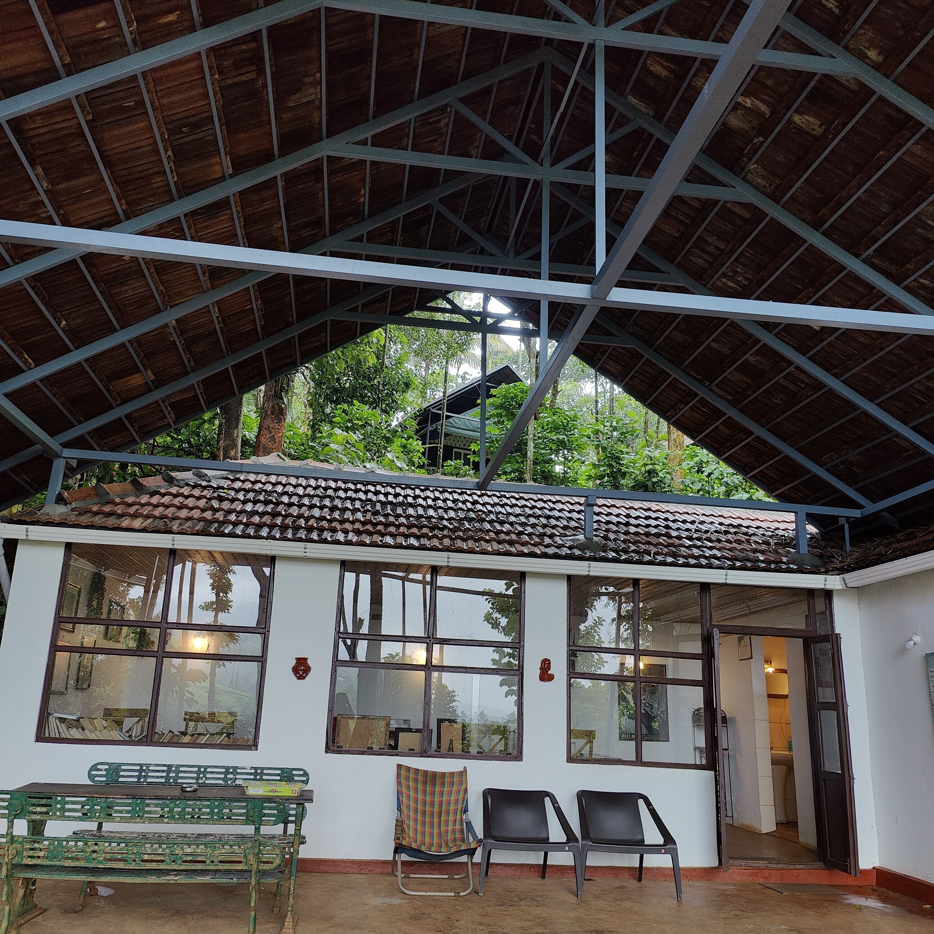 A covered outdoor area with a tiled roof, a bench, two chairs, and a small table.