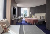 A hotel room with a bed, a desk, a chair, a TV, and a view of the city.