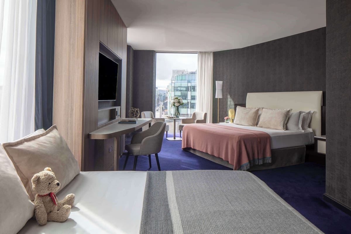 Habitación de hotel con cama, escritorio, silla, televisor y vista a la ciudad.
