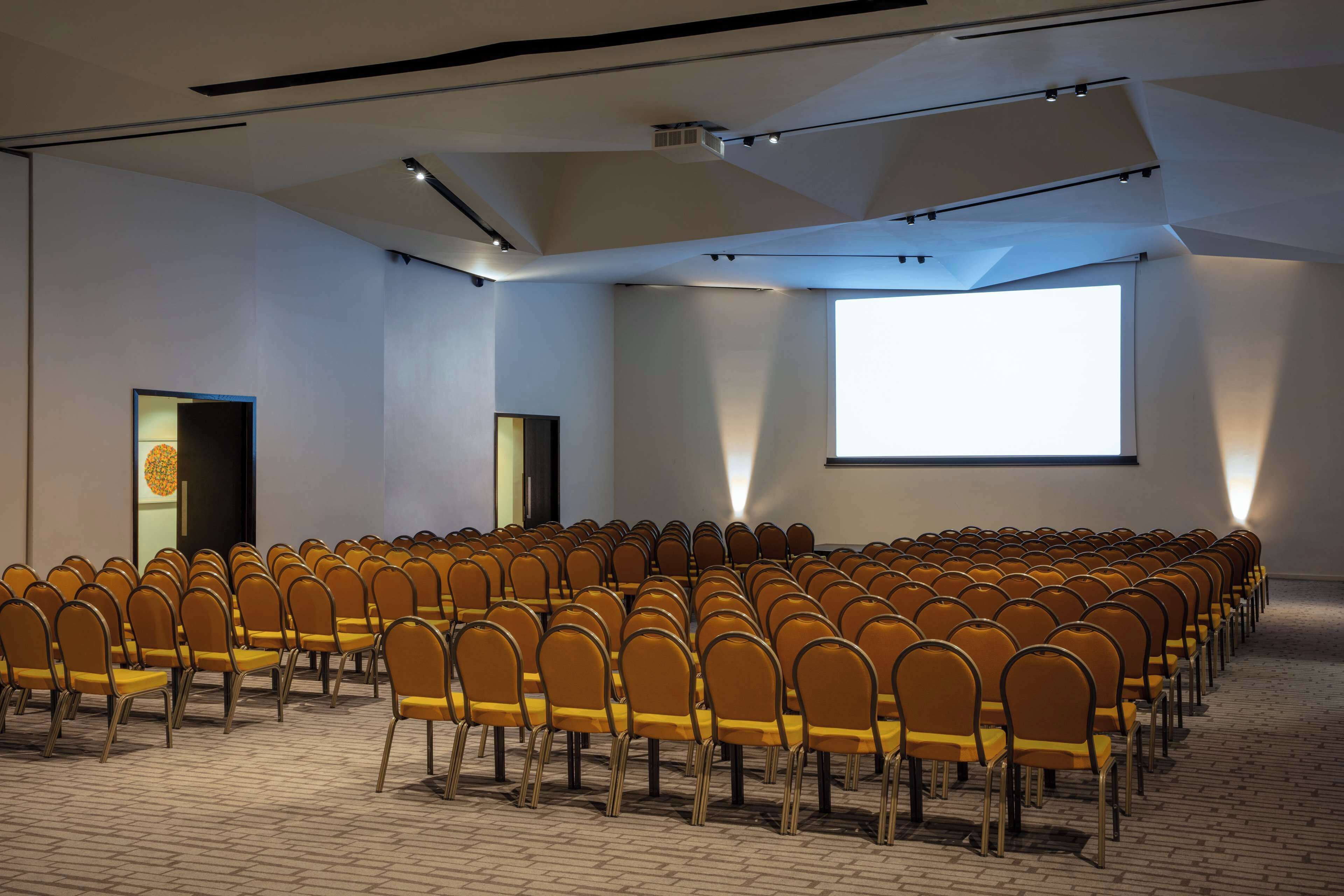 Ein Konferenzraum mit Reihen von Stühlen, einer Projektionsleinwand und einem großen Fenster.