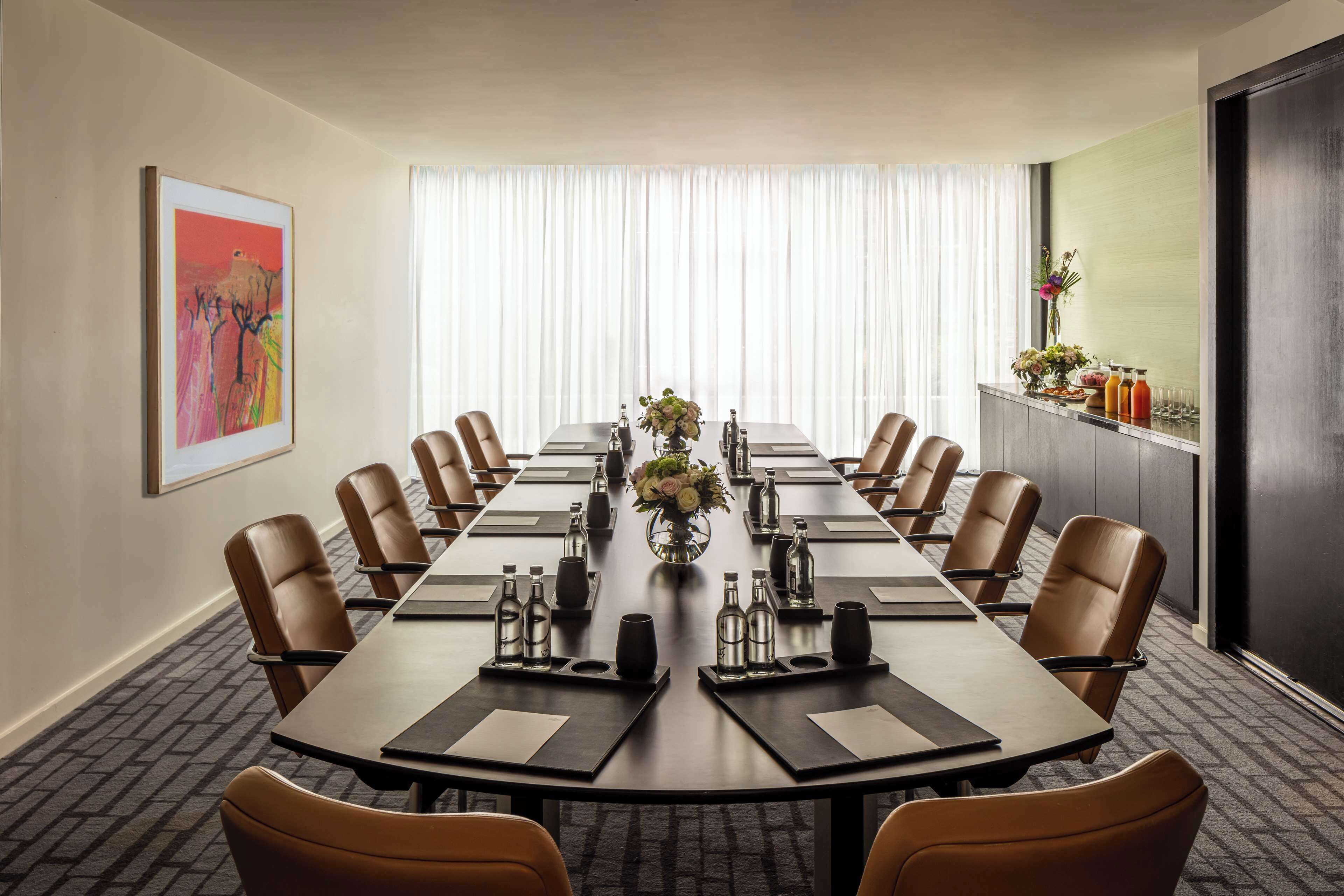 A conference room with a long table, brown leather chairs, a vase with flowers, and a painting on the wall.