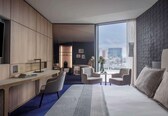 A modern hotel room with a large bed, a desk, and a view of the city.