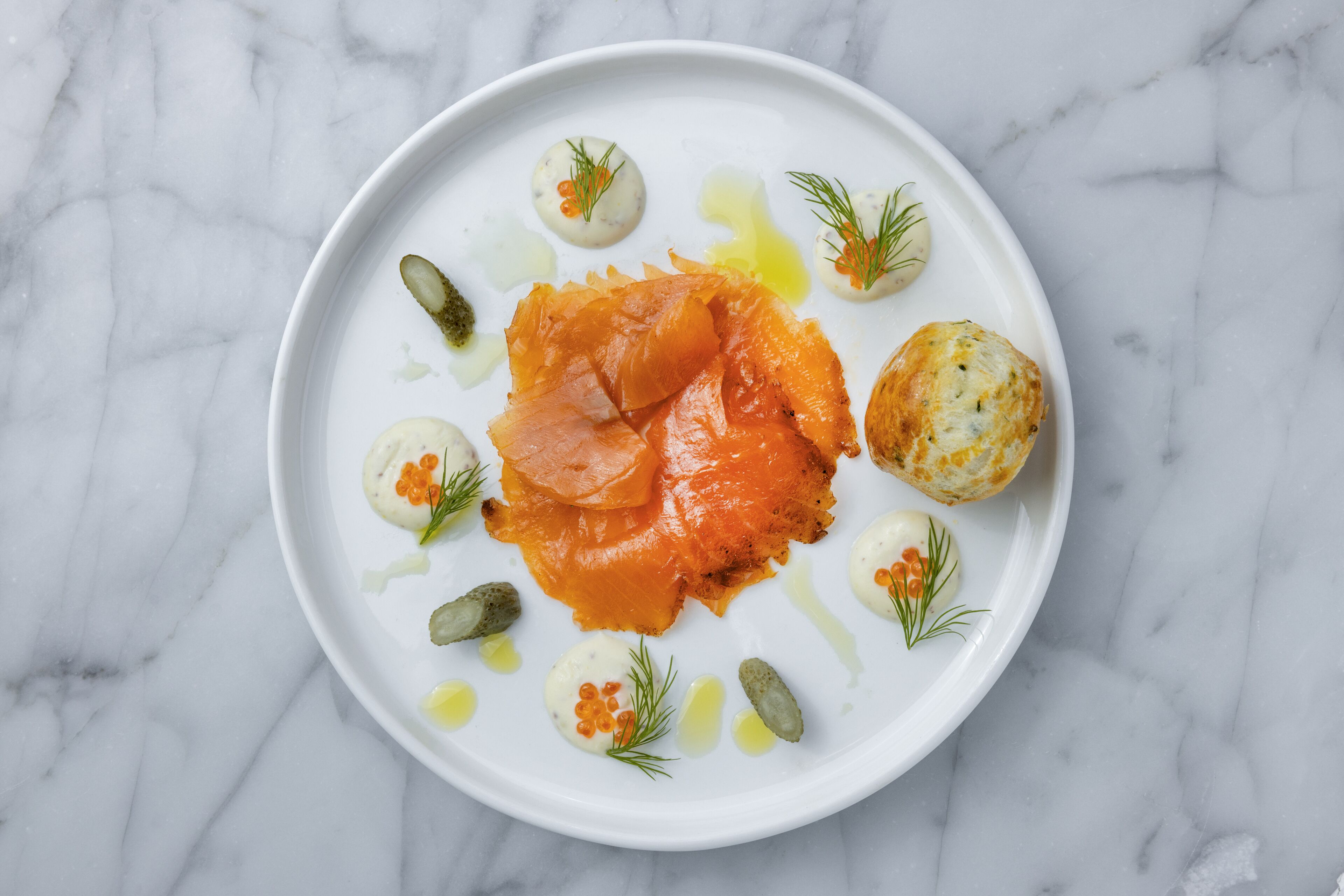 A plate of food with salmon, eggs, and garnishes on a marble surface.