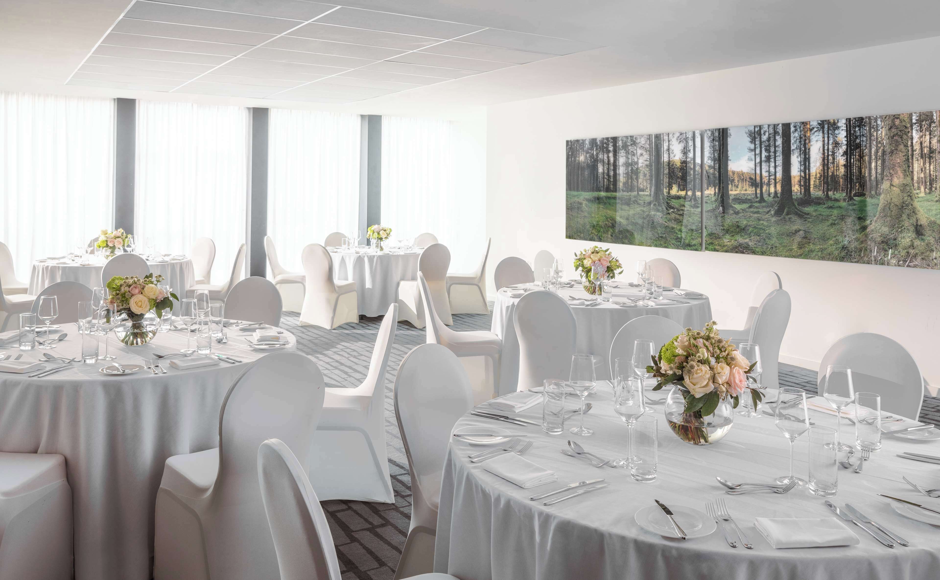 A hotel dining area with round tables, white chairs, and floral centerpieces.