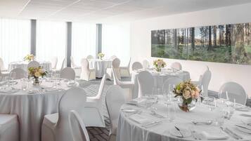 A hotel dining area with round tables, white chairs, and floral centerpieces.