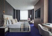 A modern hotel room with a large bed, a desk, a TV, and a sofa.