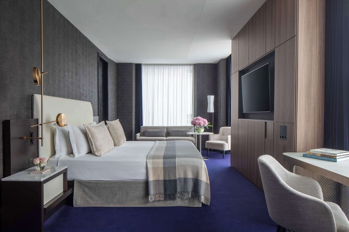 Una habitación de hotel moderna con una cama grande, un escritorio, un televisor y un sofá.