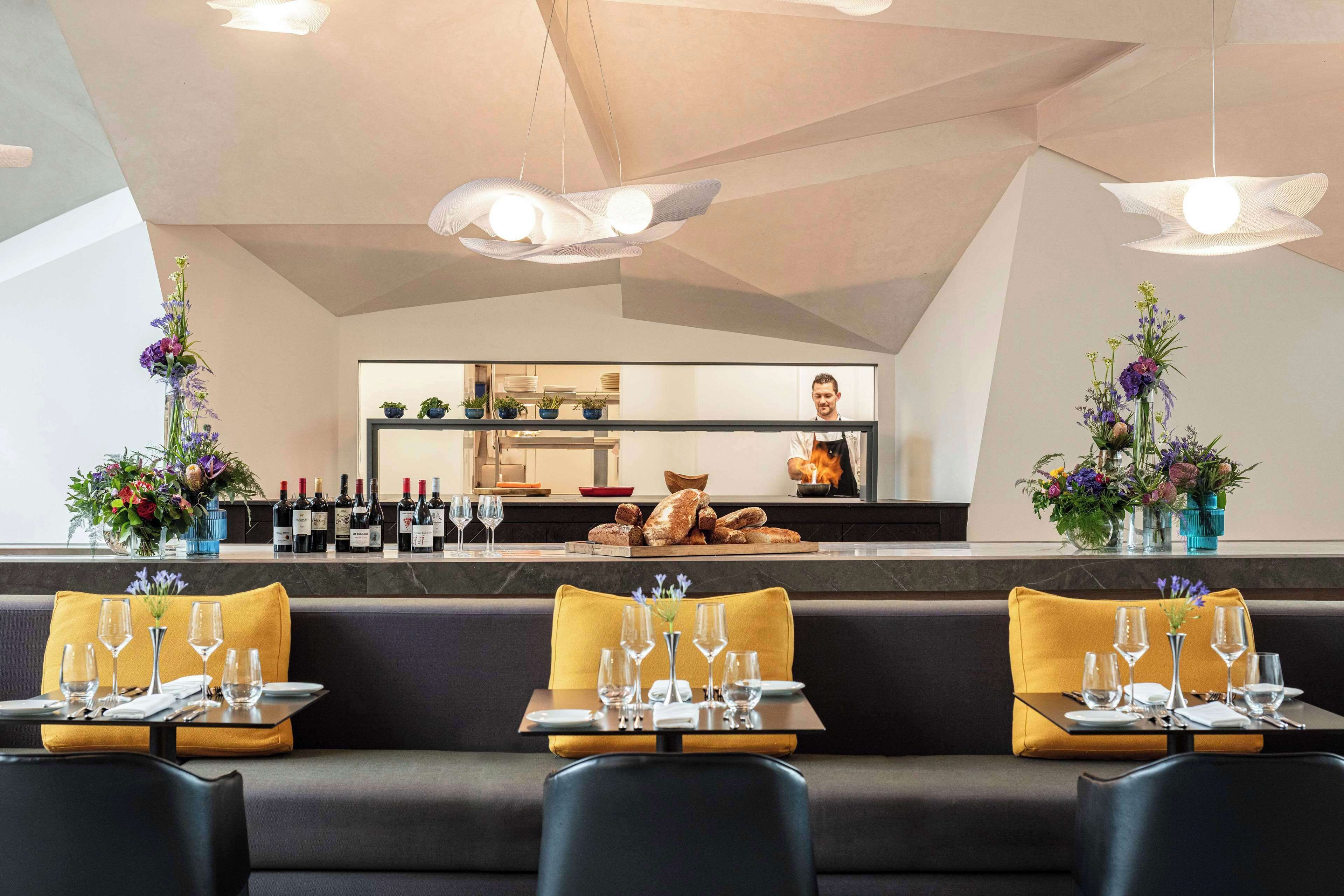 Un restaurant au décor moderne, avec un bar, des sièges dotés de coussins jaunes et une variété de fleurs.