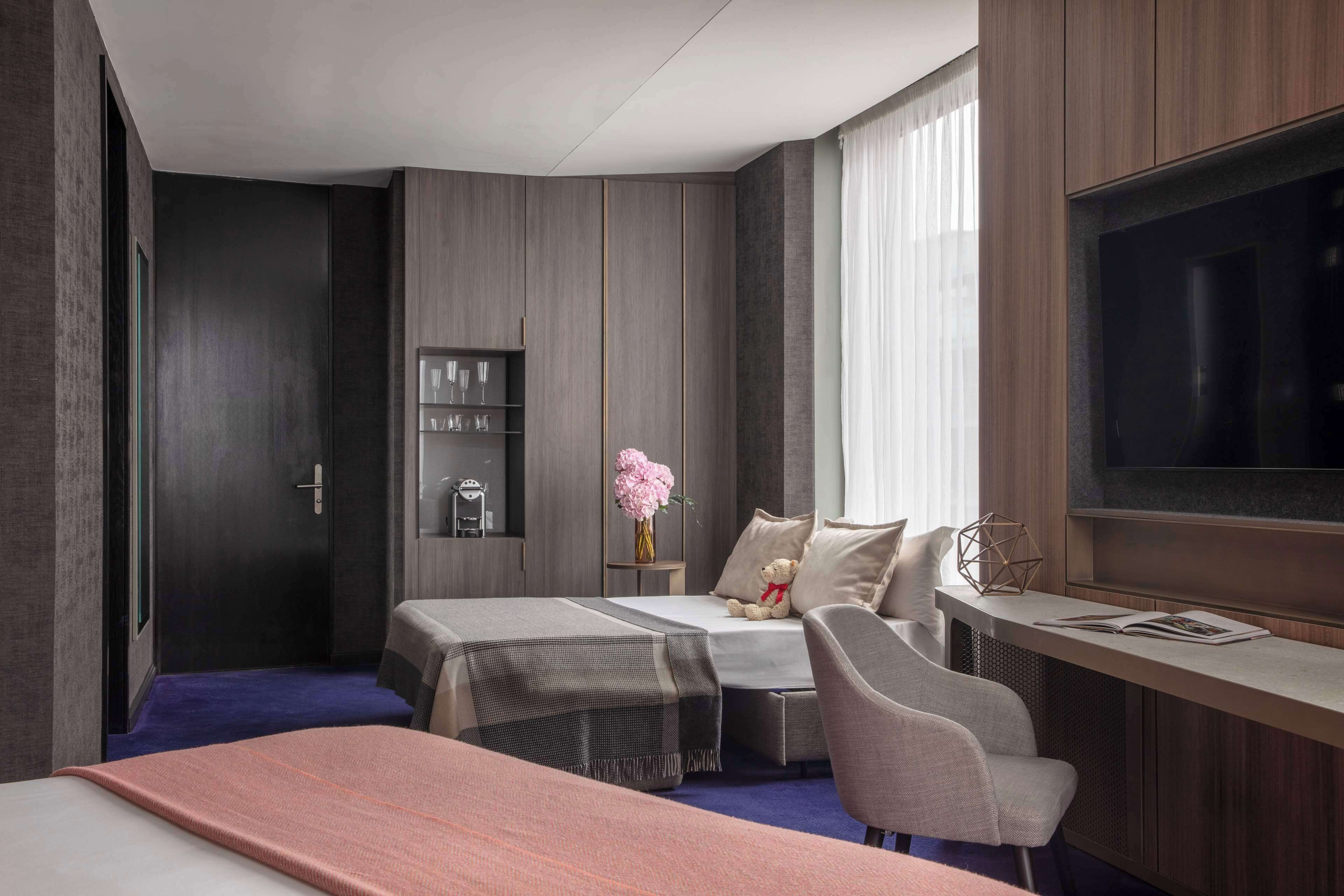 A modern hotel room with a large bed, a desk with a chair, a TV, and a small seating area with a sofa and a table.