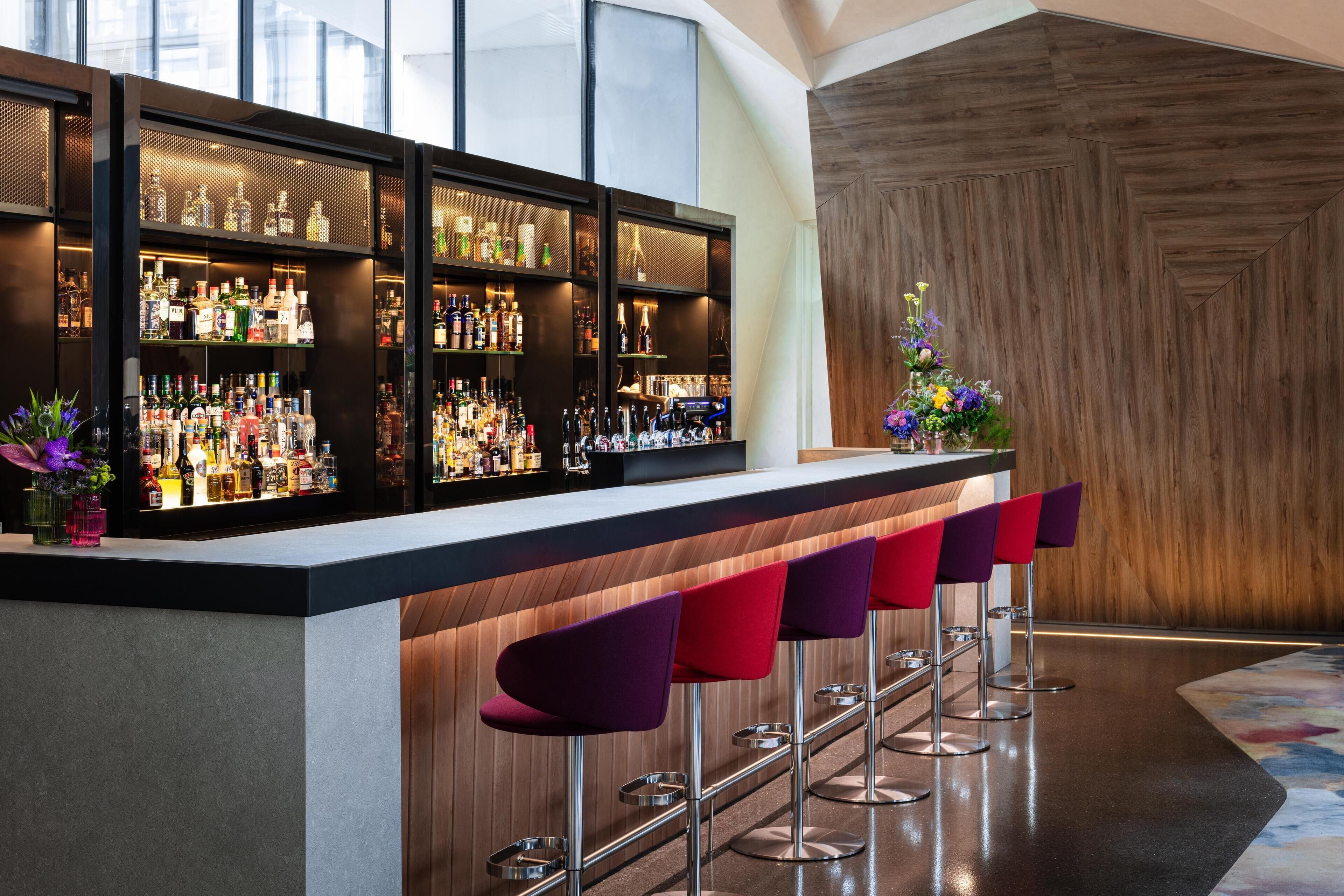 A bar area with multiple shelves of liquor bottles, a bar counter, and several bar stools.