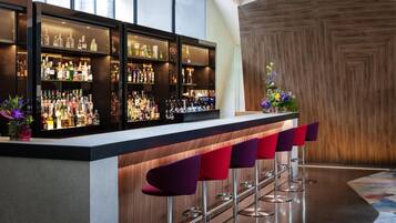 A bar area with multiple shelves of liquor bottles, a bar counter, and several bar stools.