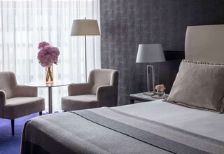 A hotel room with a bed, two armchairs, a small table with a vase of flowers, and a lamp.