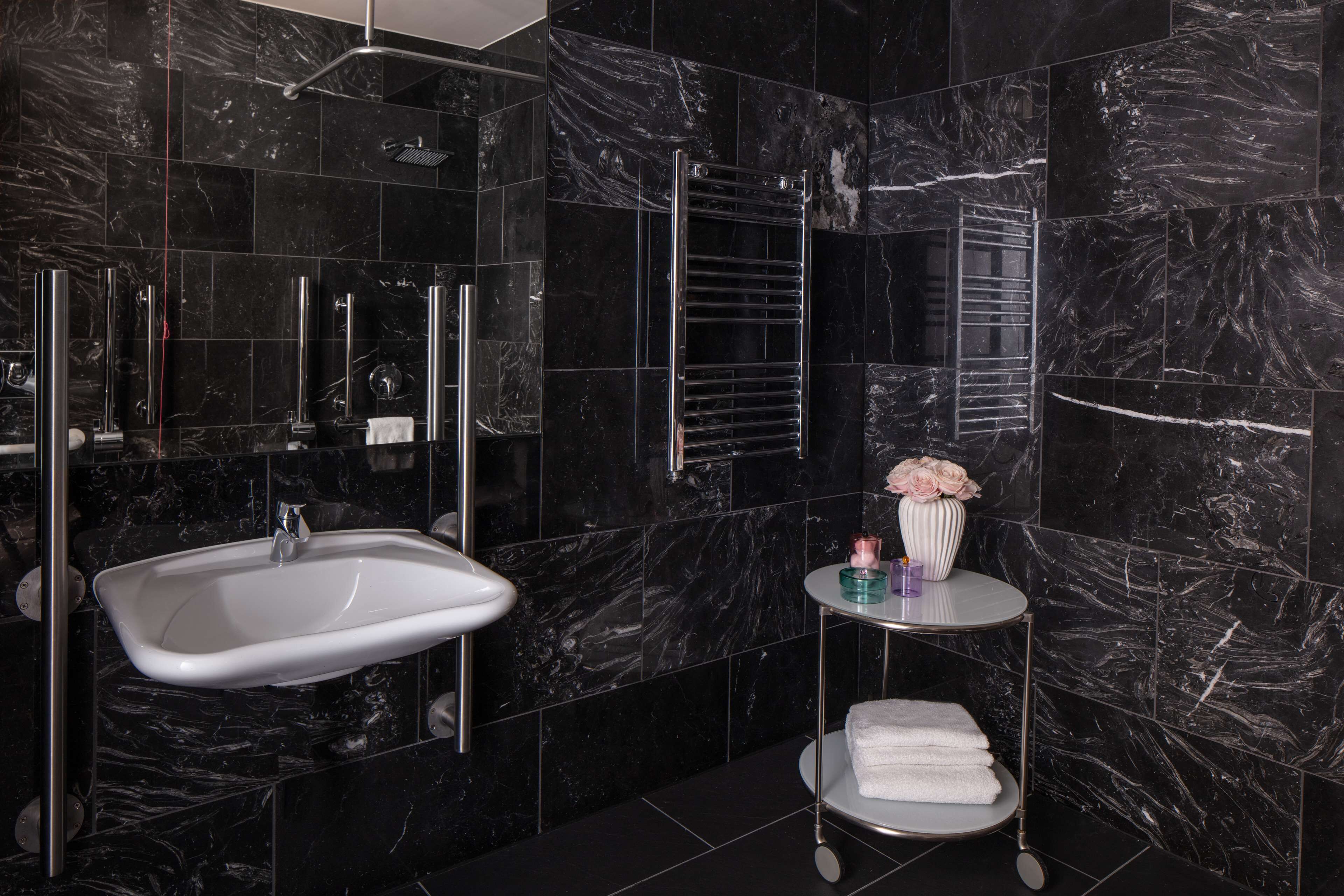 A modern bathroom with a white sink, a glass shower enclosure, and a small round table with a vase and towels.