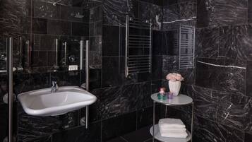 A modern bathroom with a white sink, a glass shower enclosure, and a small round table with a vase and towels.