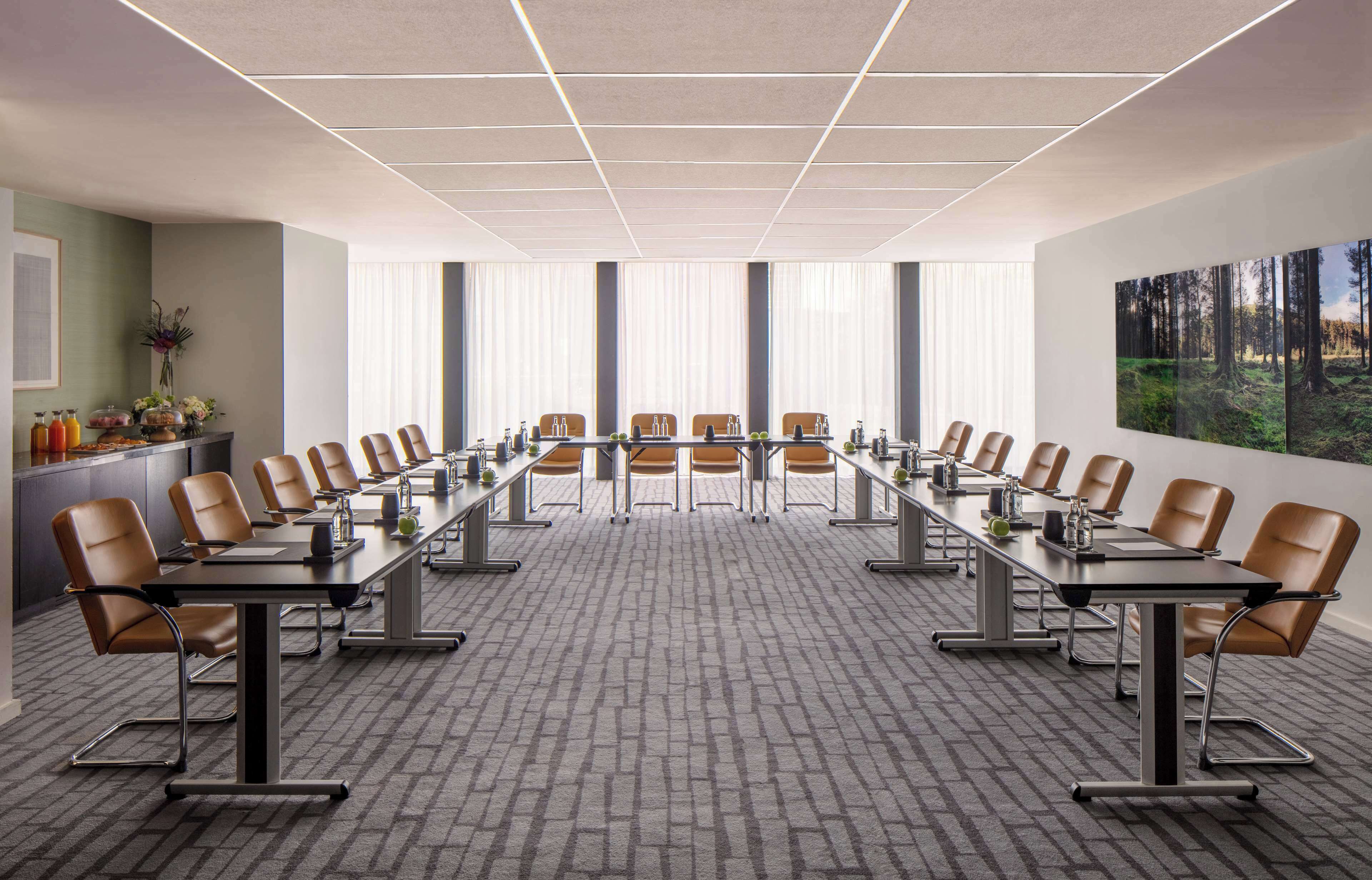 A conference room with a long table, chairs, and a view of a forest through large windows.