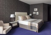 A modern hotel room with a large bed, two bedside tables, a chair, and a dark textured wall.