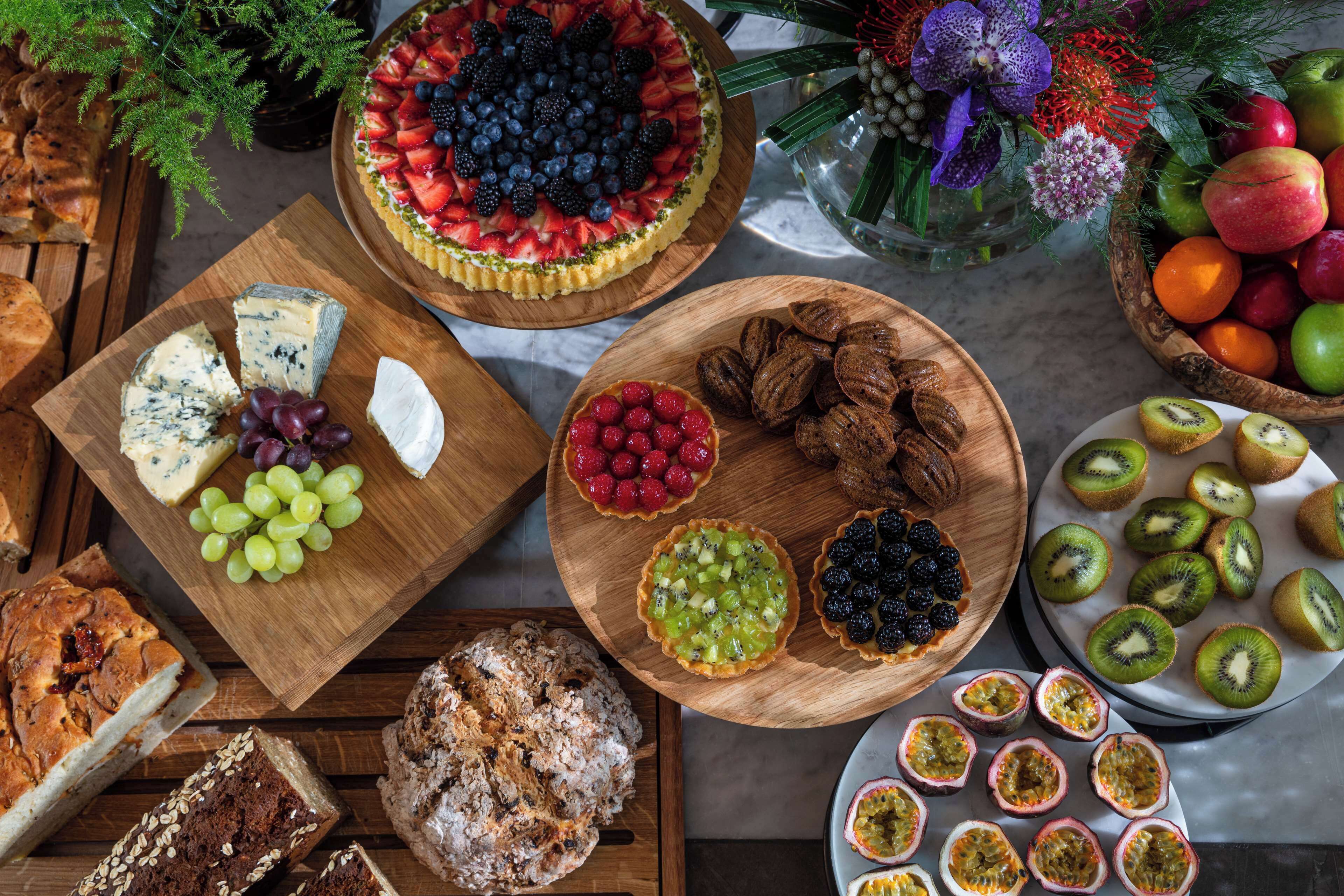 A variety of food items including cheese, fruits, and pastries on wooden boards.