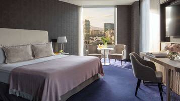 A modern hotel room with a large bed, a desk, and a view of a cityscape.