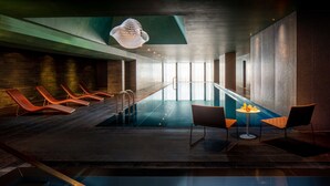 Una piscina interior moderna con sillones de descanso, una mesa con fruta y una lámpara colgante original.