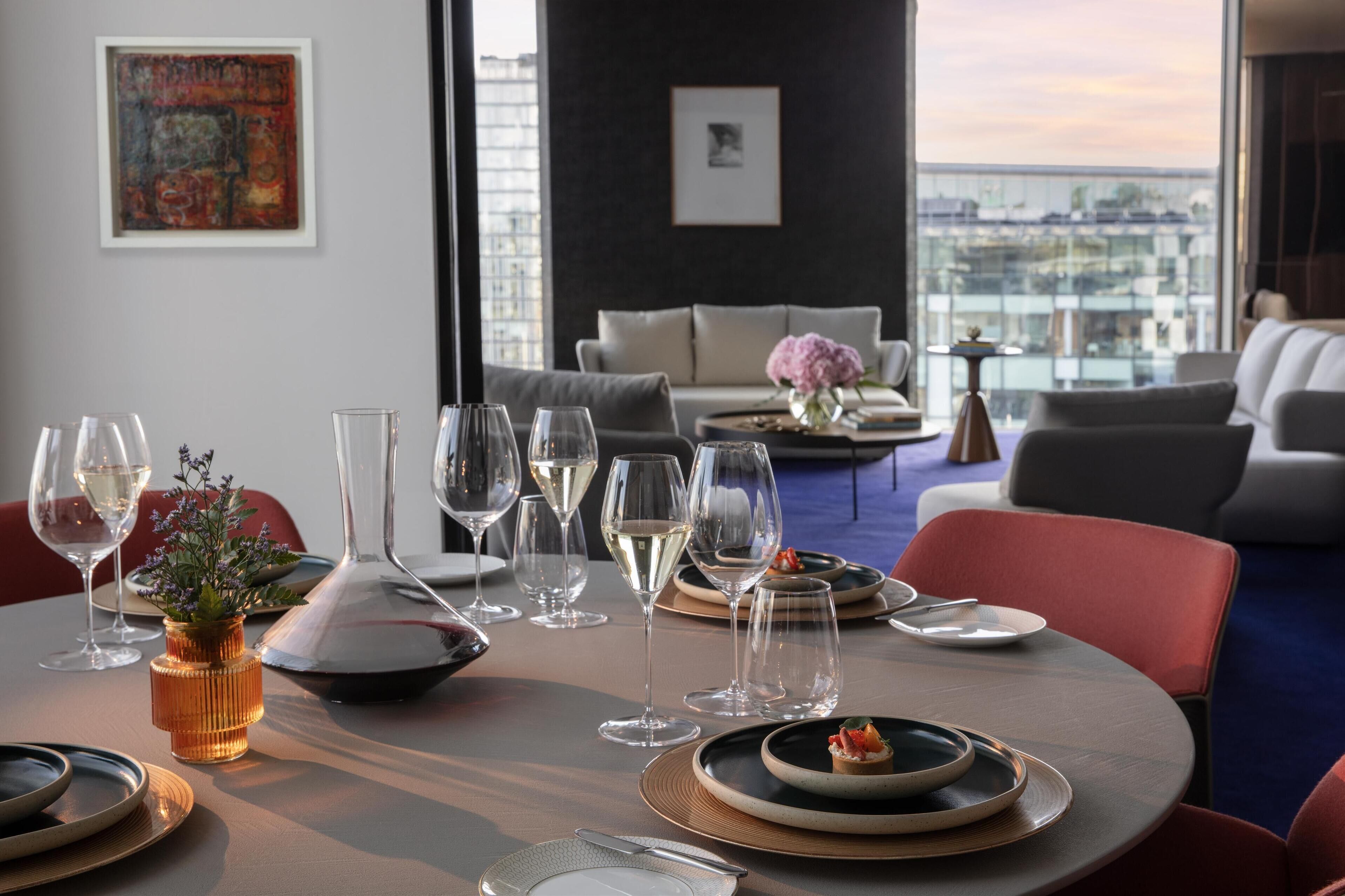 A dining area with a table set for a meal, glasses, and a vase with flowers.