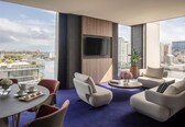 A modern living room with a city view, a flat-screen TV, and a dining area with a table set for two.
