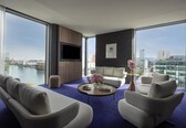 A modern hotel room with a large window, a flat-screen TV, a sofa, a coffee table, and a view of the city.