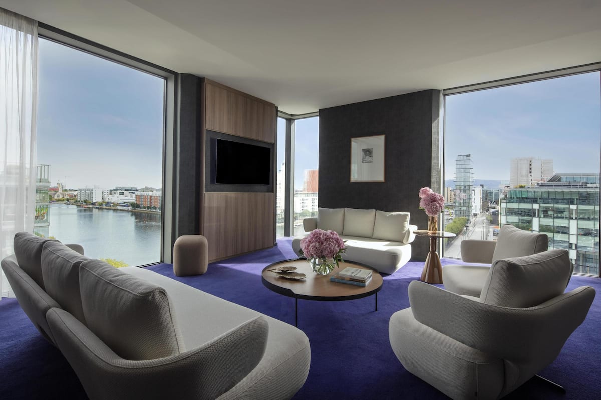 Una habitación de hotel moderna con un amplio ventanal, un televisor de pantalla plana, un sofá, una mesa de centro y vistas a la ciudad.