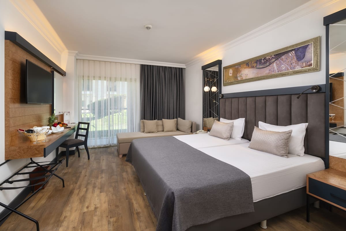A modern hotel room with a large bed, a desk with a chair, a flat-screen TV, and a large window with curtains.