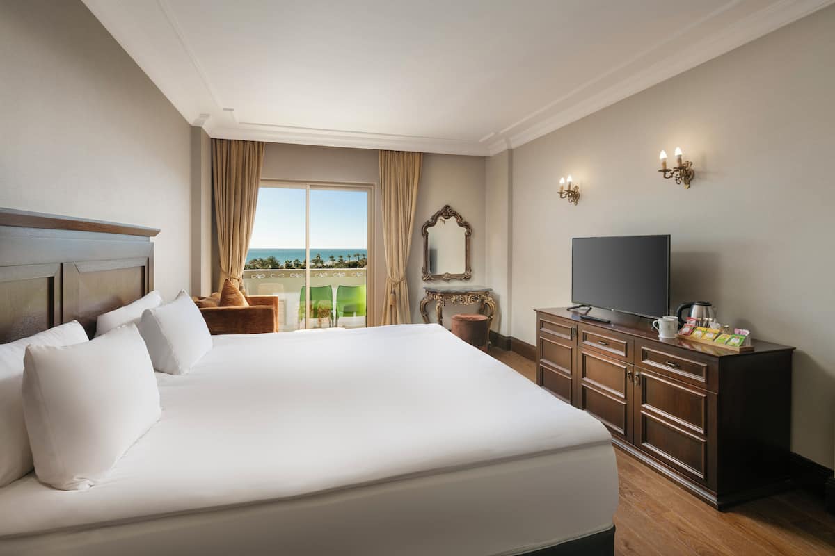 A hotel room with a large bed, a television, a dresser, and a view of the ocean.