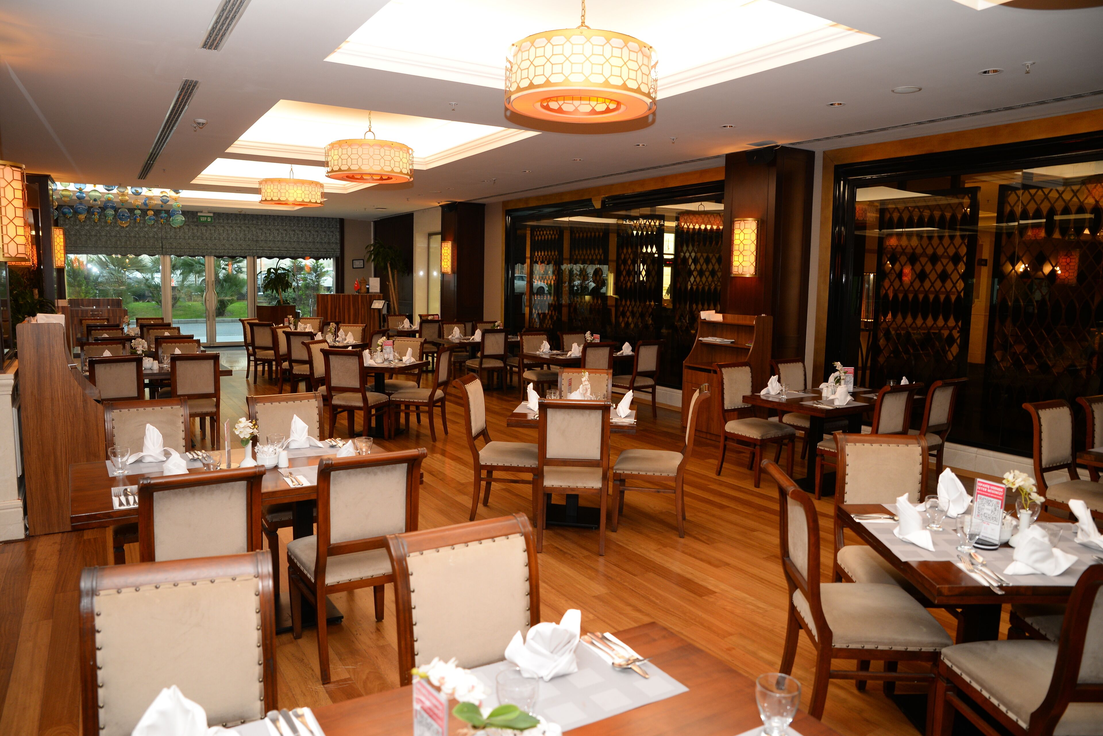 A spacious restaurant with multiple dining tables and chairs, large windows, and decorative lighting.