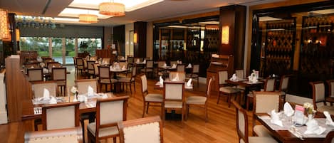A spacious restaurant with multiple dining tables and chairs, large windows, and decorative lighting.
