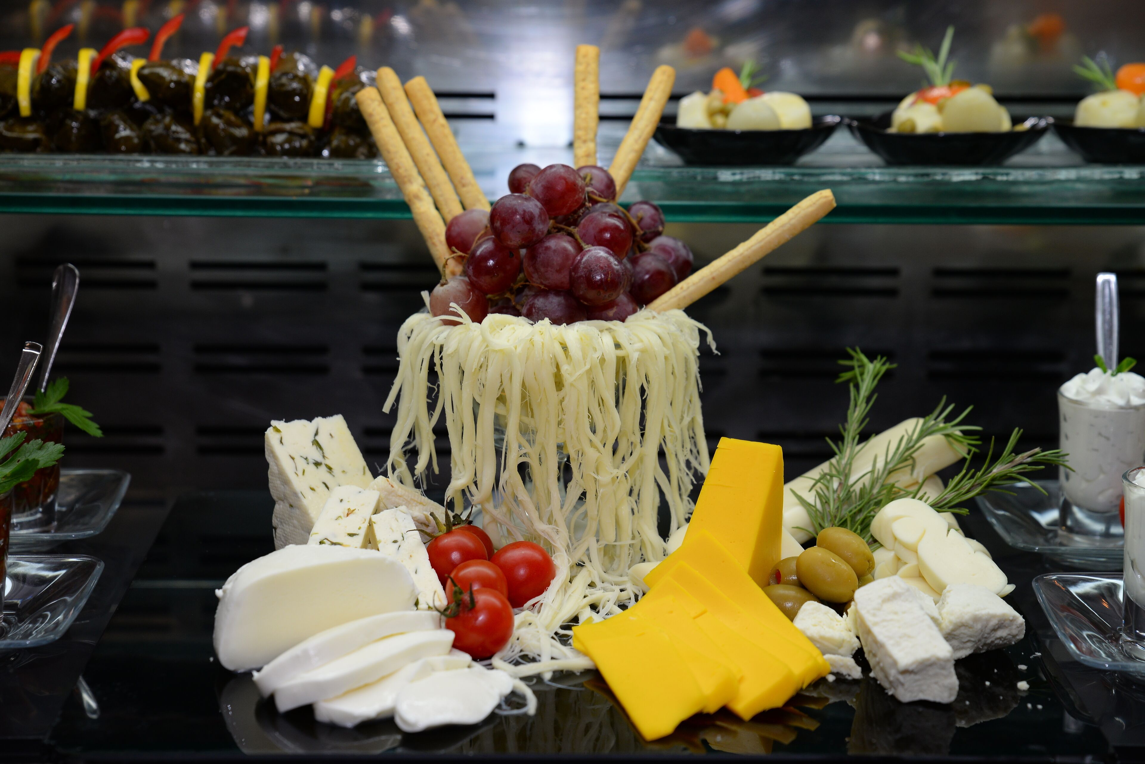 A buffet with various cheeses, grapes, and vegetables.