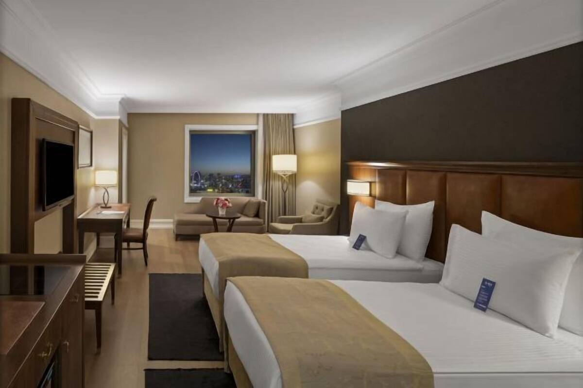A hotel room with two beds, a desk, a chair, a TV, and a window with a city view.