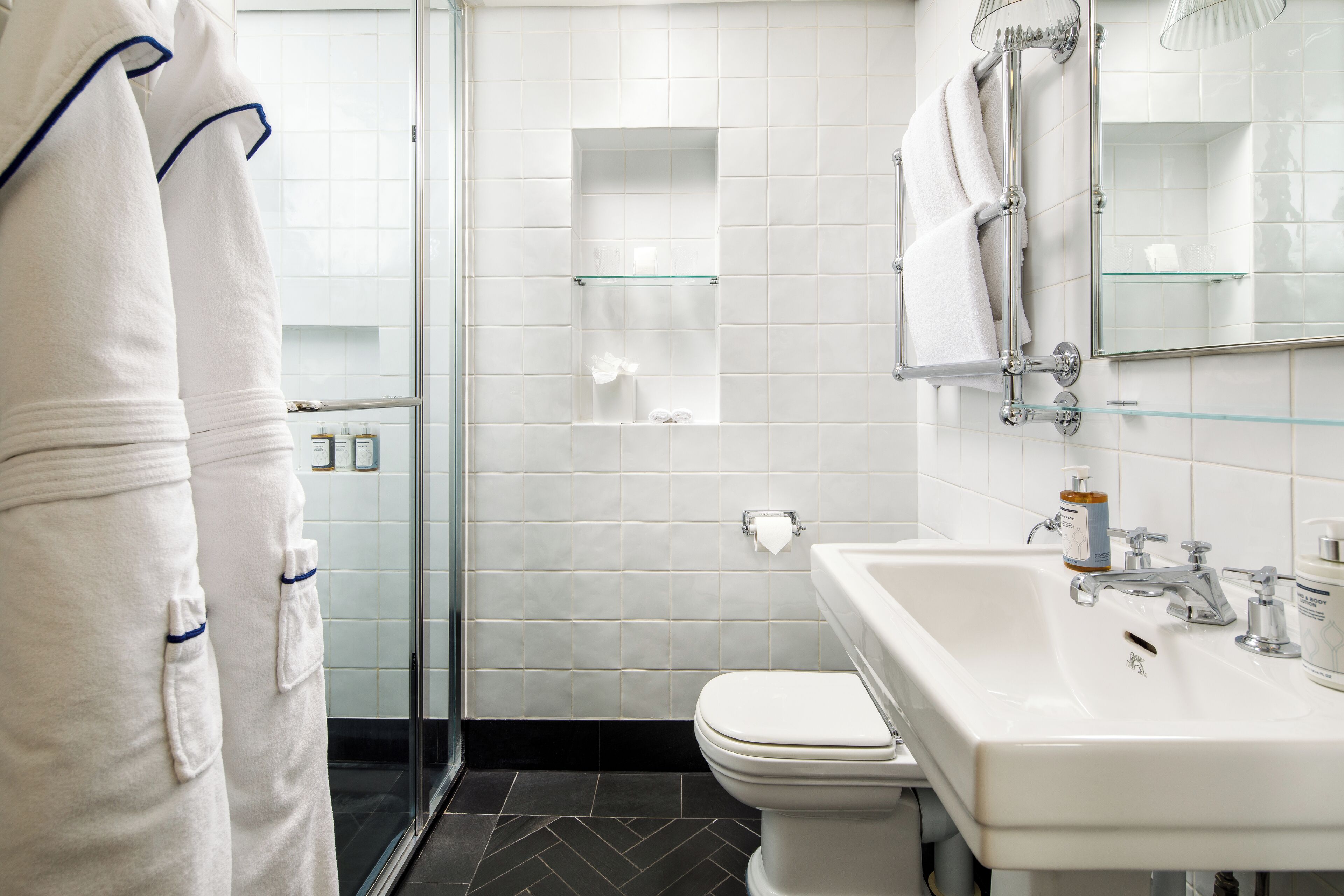 Ein Badezimmer mit Duschkabine aus Glas, einem weißen Waschbecken mit Spiegel und einer Toilette.