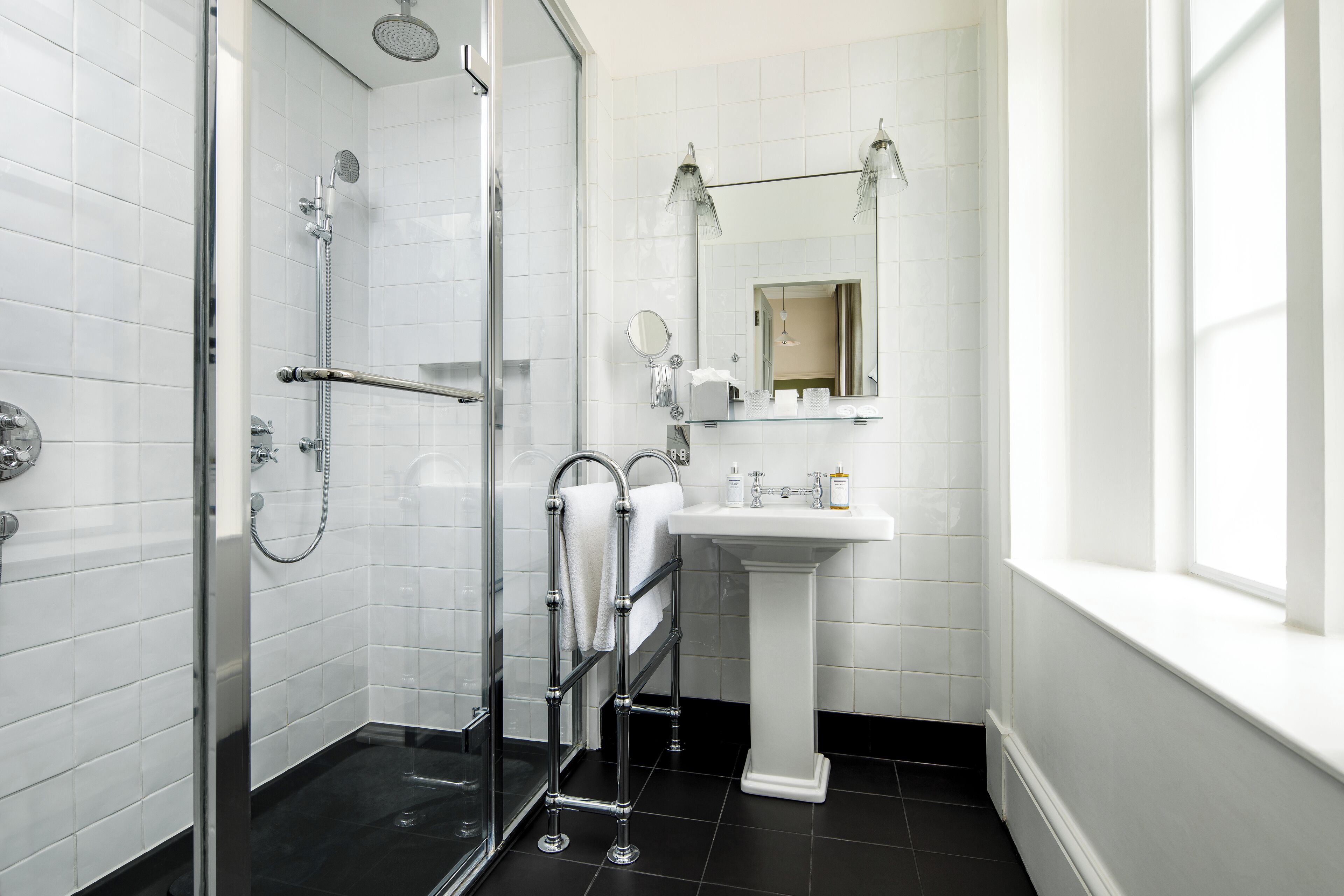 A modern bathroom with a glass shower enclosure, a white pedestal sink, and a large mirror above the sink.