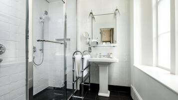 A modern bathroom with a glass shower enclosure, a white pedestal sink, and a large mirror above the sink.