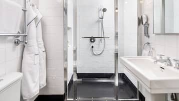 Ein modernes Badezimmer mit einer in Glas eingefassten Dusche, weißen Fliesen, einem weißen Waschbecken und einem Spiegel.
