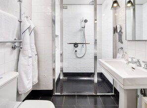 A modern bathroom with a glass-enclosed shower, white tiles, a white sink, and a mirror. - Kaya Great Northern Hotel (London)