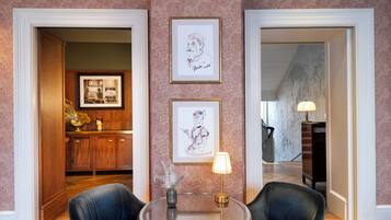 A room with a round table, two chairs, framed artwork on the wall, and a wooden cabinet.