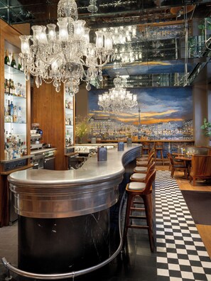 A bar area with a large black marble bar, multiple wooden chairs, a checkered floor, and a cityscape mural on the wall. - Kaya Great Northern Hotel (London)