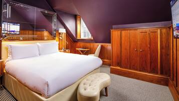 A bedroom with a large bed, a wooden wardrobe, a small table, and a chair.