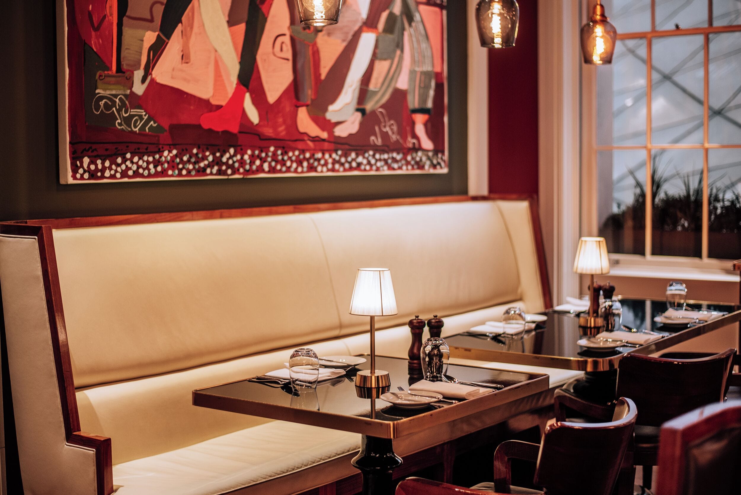 A restaurant interior with a long wooden table set for dining, a cushioned bench, and pendant lighting.