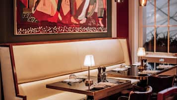A restaurant interior with a long wooden table set for dining, a cushioned bench, and pendant lighting.