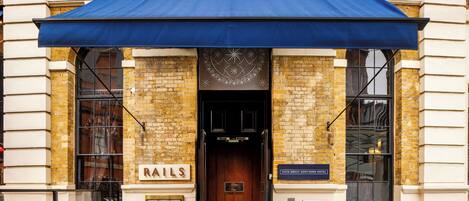 A hotel entrance with a blue awning, a wooden door, and a sign that reads "RAILS".