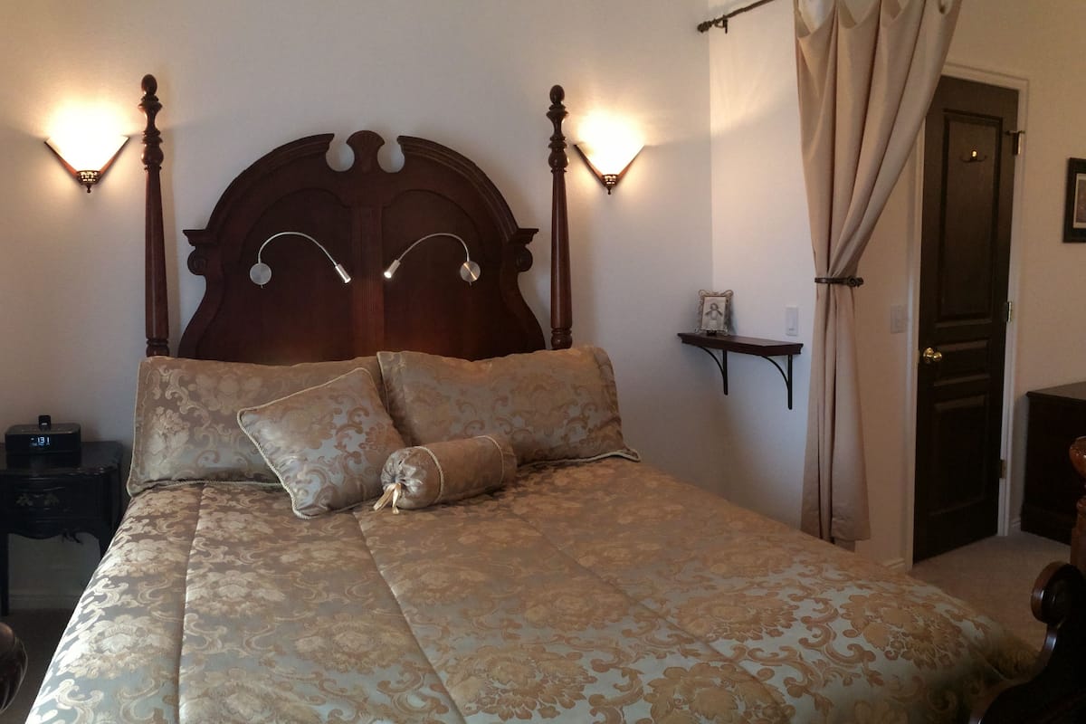 A bedroom with a large bed, two wall-mounted lamps, a bedside table, a nightstand, and a door.