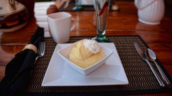 A dessert in a white bowl on a square plate, with a fork and knife beside it on a placemat.