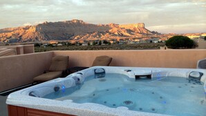 A hot tub with jets, a chair, and a table on a rooftop with a mountain view.